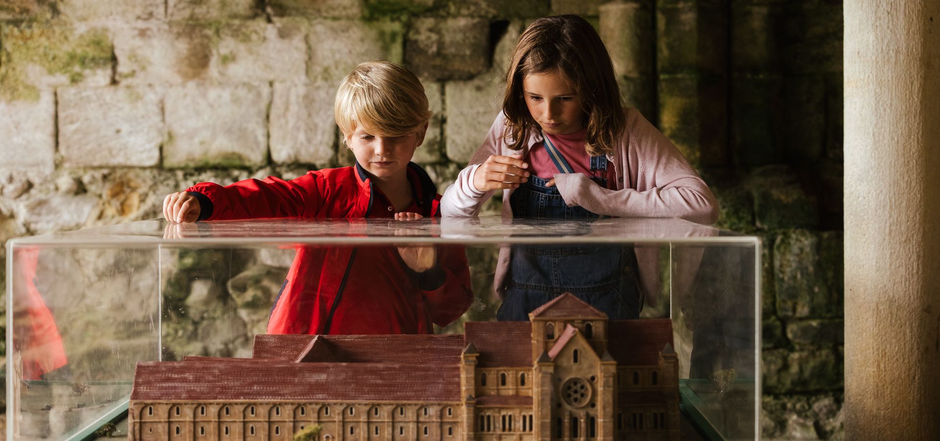 two children looking down into a display cabinet with a replica building in