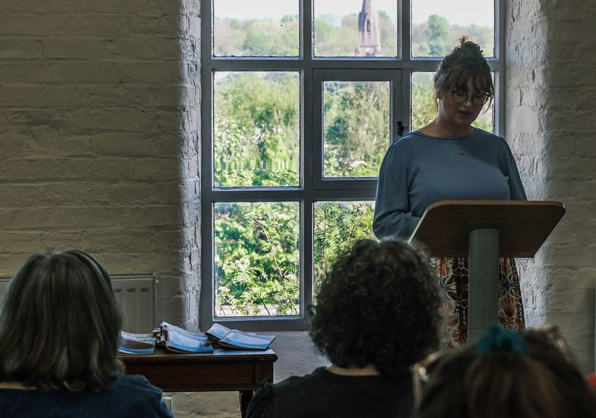 Woman reading from lectern in front of a window to an audience