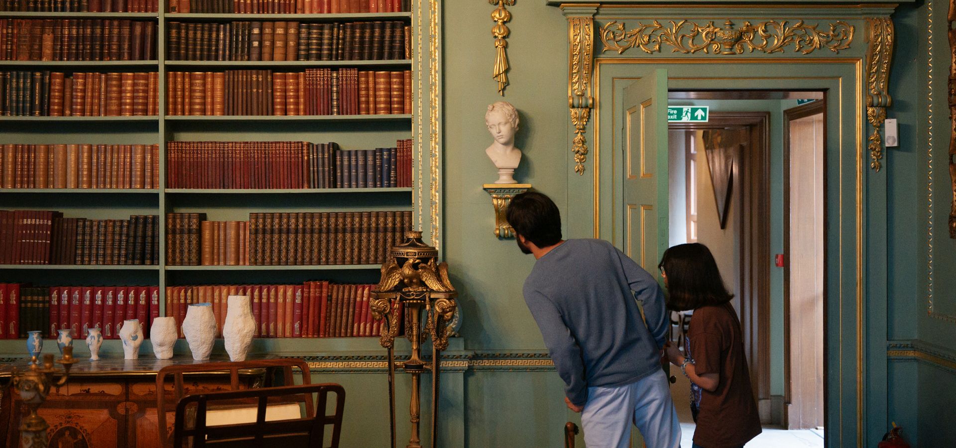 An adult and child looking at a teal wall covered in books next to a doorway