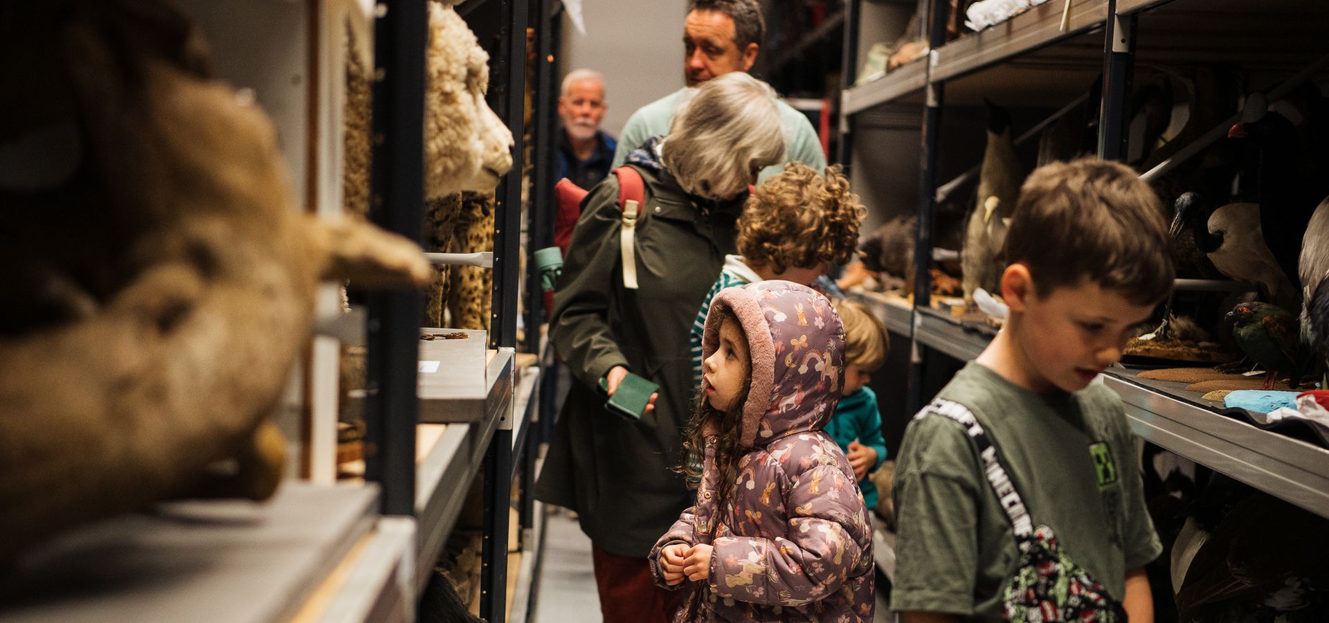 3 children working down a aisle in Leeds Discovery Centre looking at shelves with natural science collections on