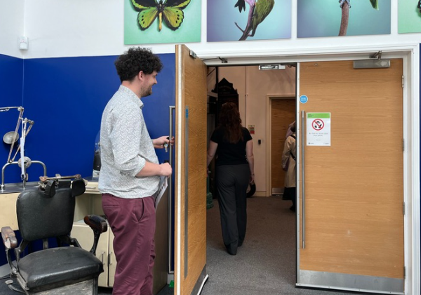 A member of staff holding open the door the the collection store for visitors to go through