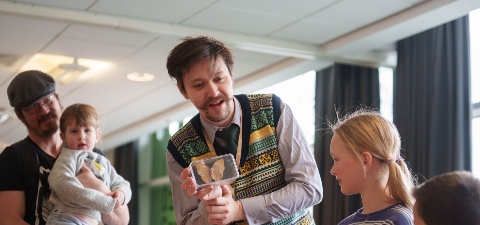 A workshop leader holding a clear box with a preserved moth in