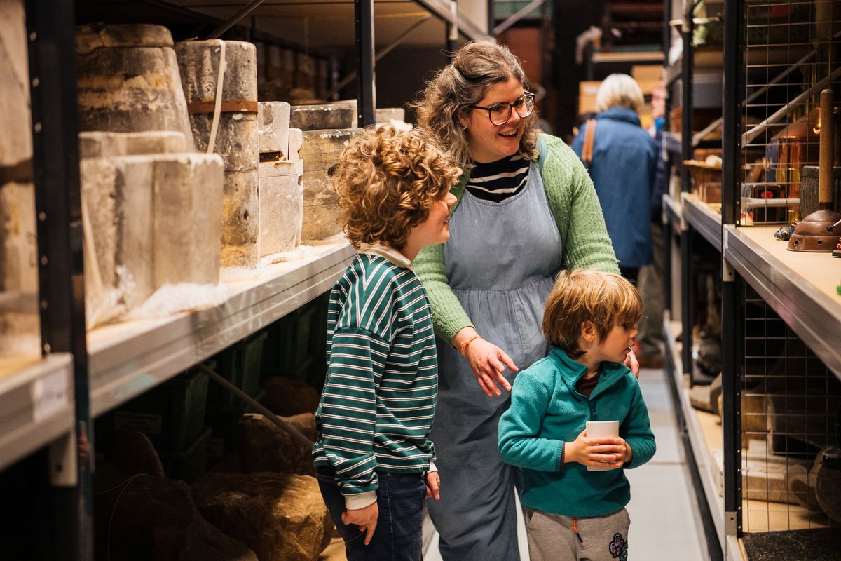 A adult and 2 children looking at museum shelving holding objects