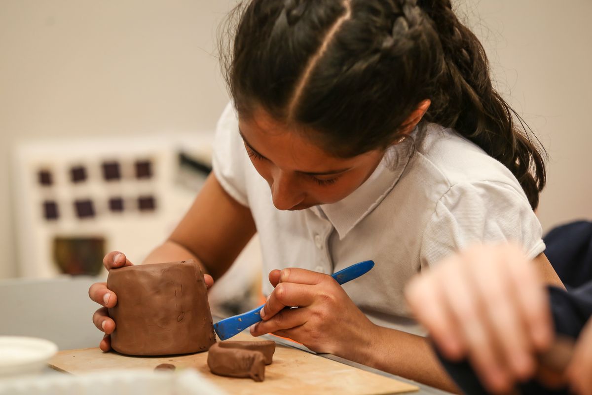 Child making a small clay pot and using a blue tool to carve patterns in to it