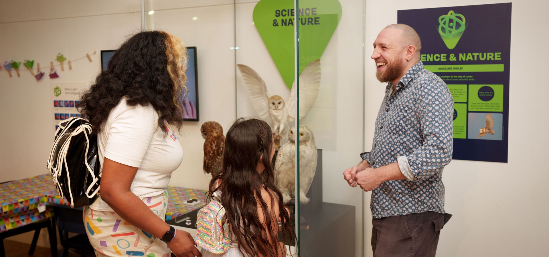 two adults and a child looking at a display case with taxidermy owls in