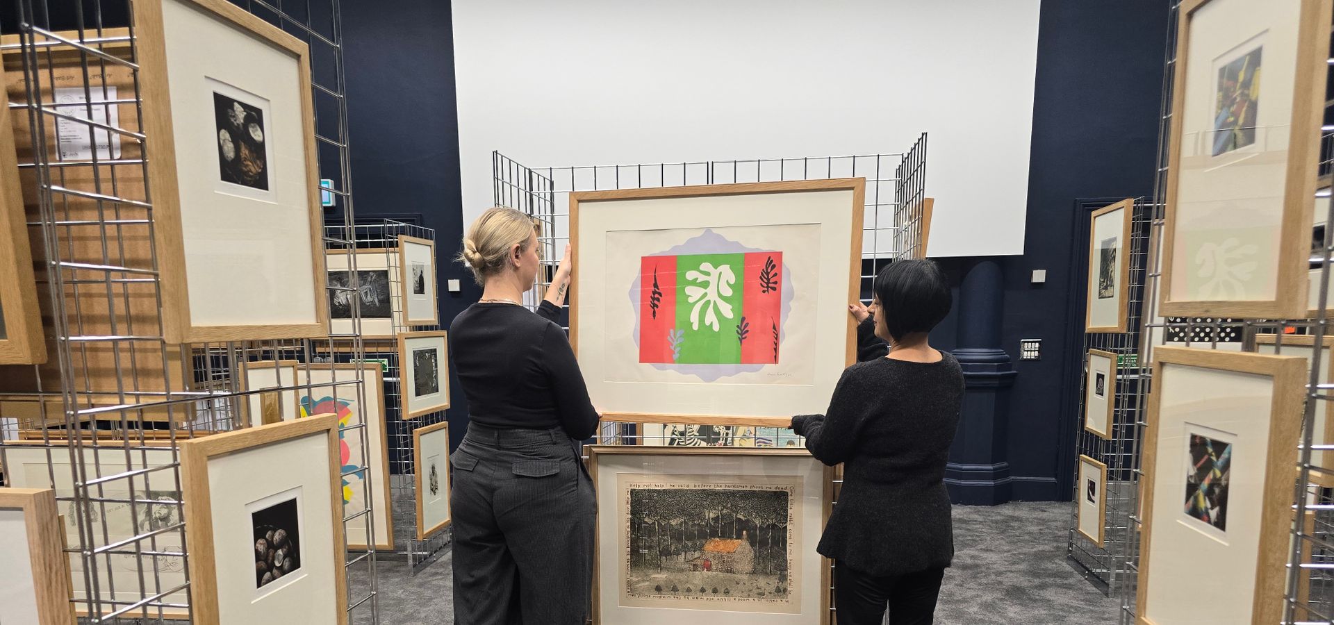 Two people hanging artwork on wire frames