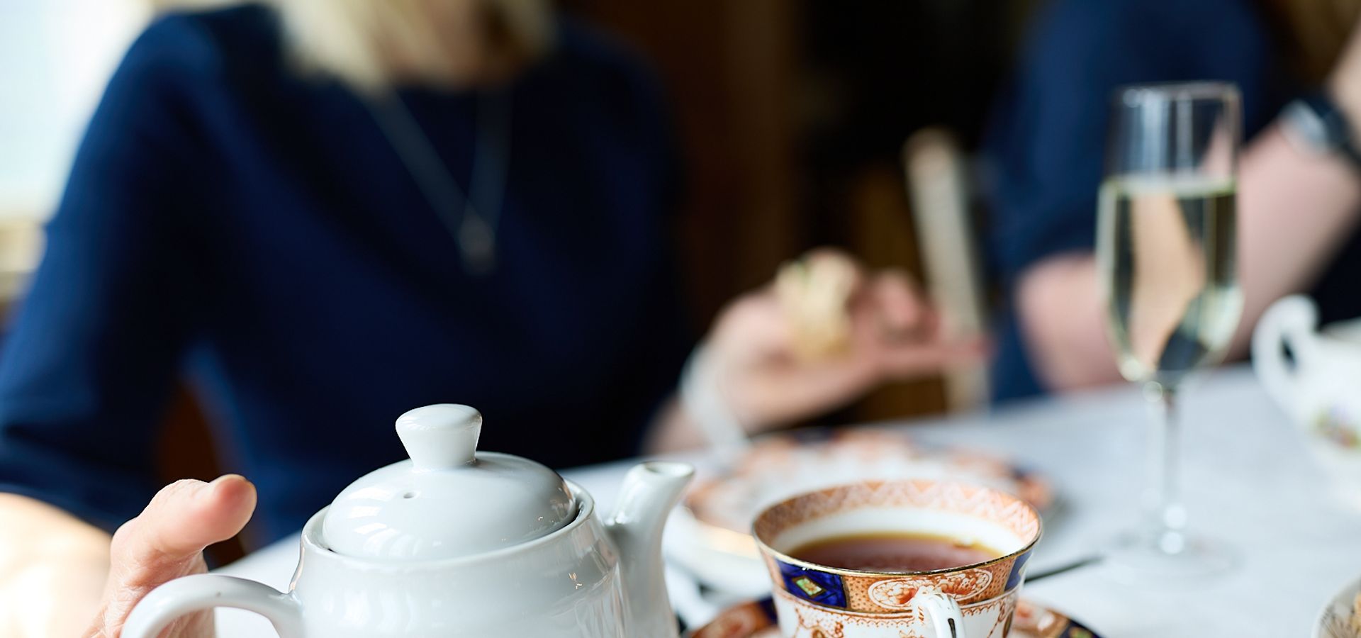 a hand reaching for a teapot next to a fine china tea cup and saucer