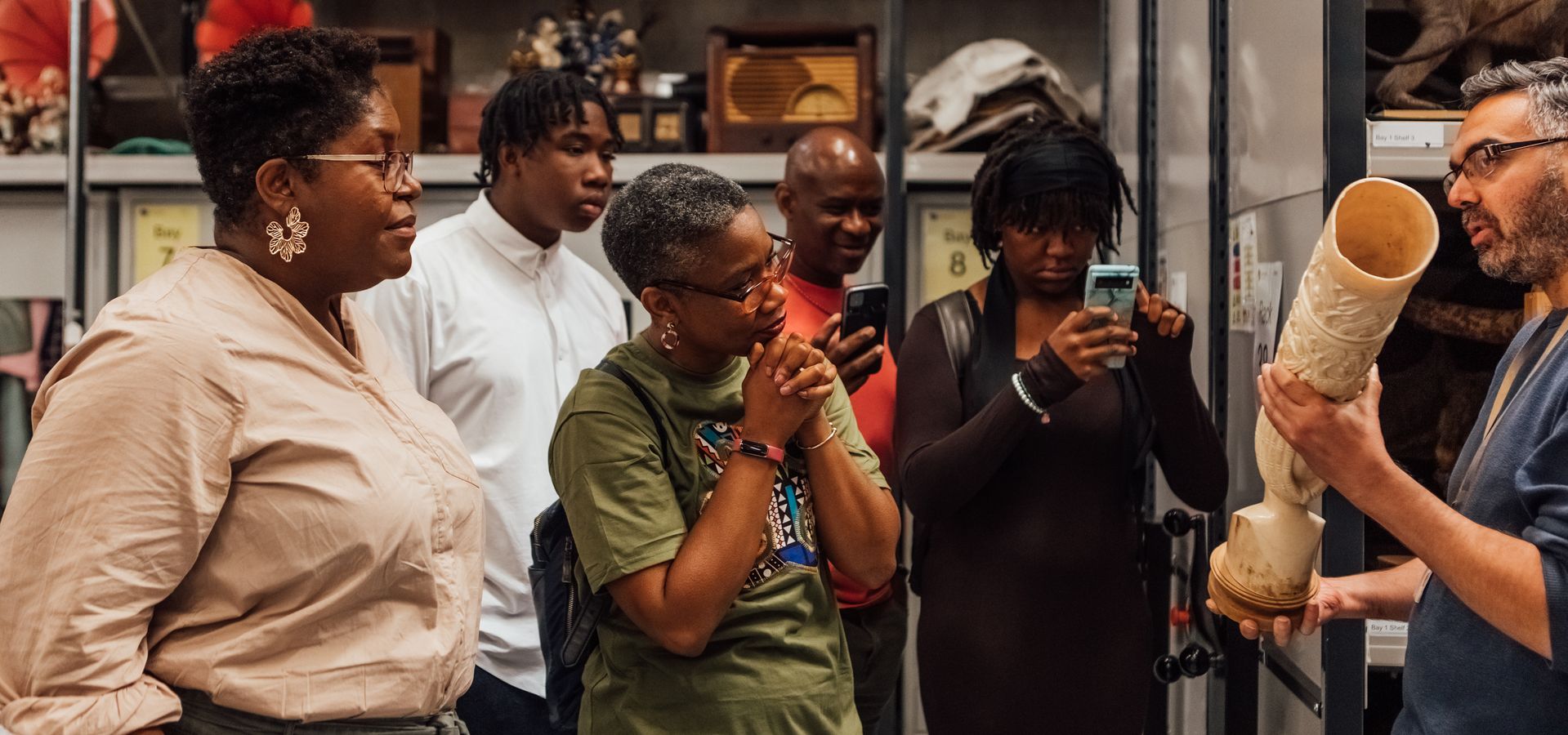 A member of staff holding a long object with a tour group standing around looking and taking pictures