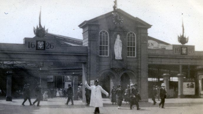 A black and white image from 1626 of a building in Leeds with a person in white walking across ringing a bell