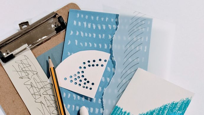 A clipboard with a pile of white and blue coloured paper with cut outs and different shapes drawn on