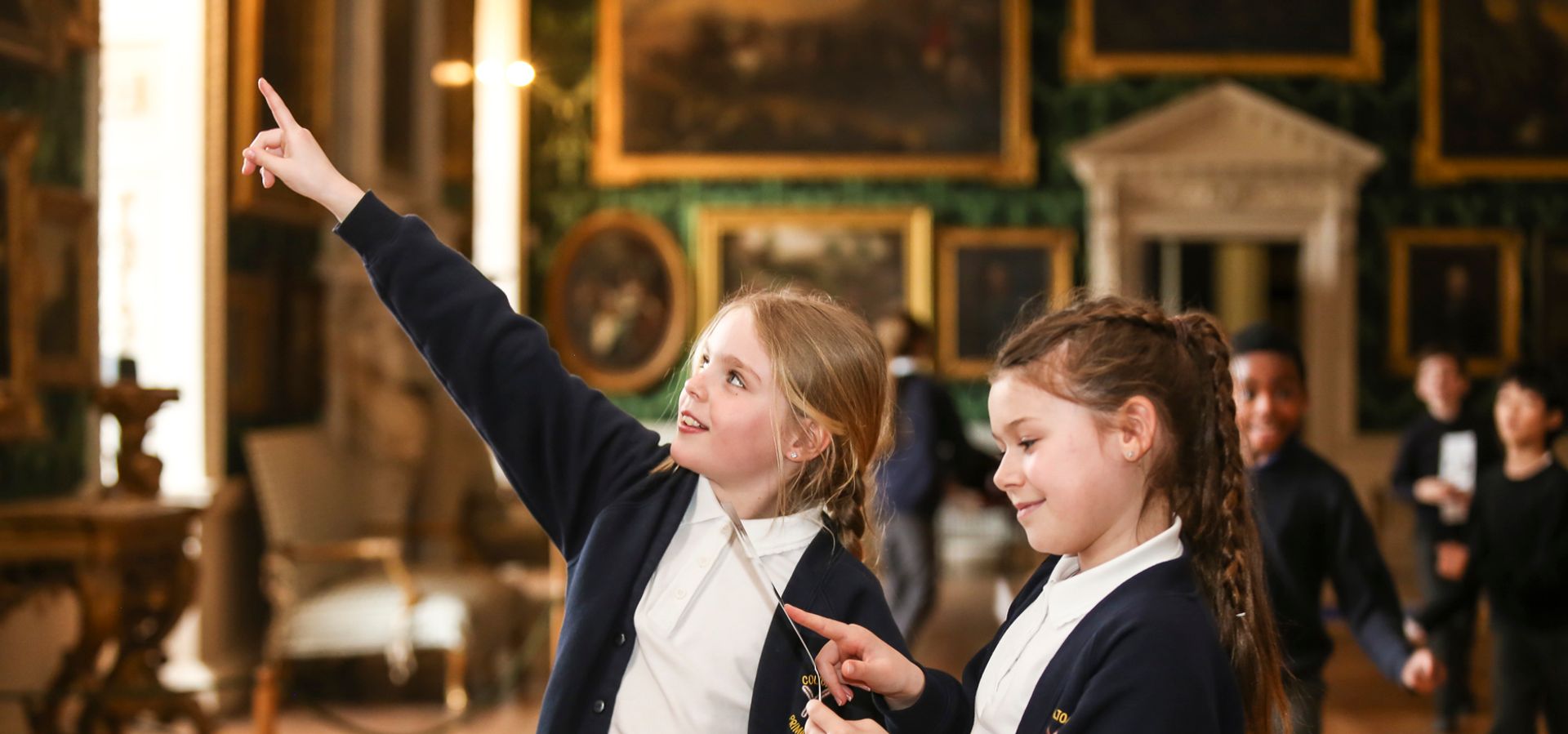 Two primary school children point at a wall of paintings at Temple Newsam house.