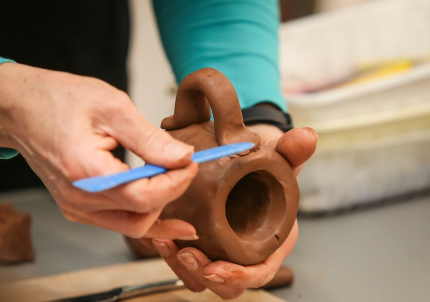 Two hands making a clay pot with a knife like tool