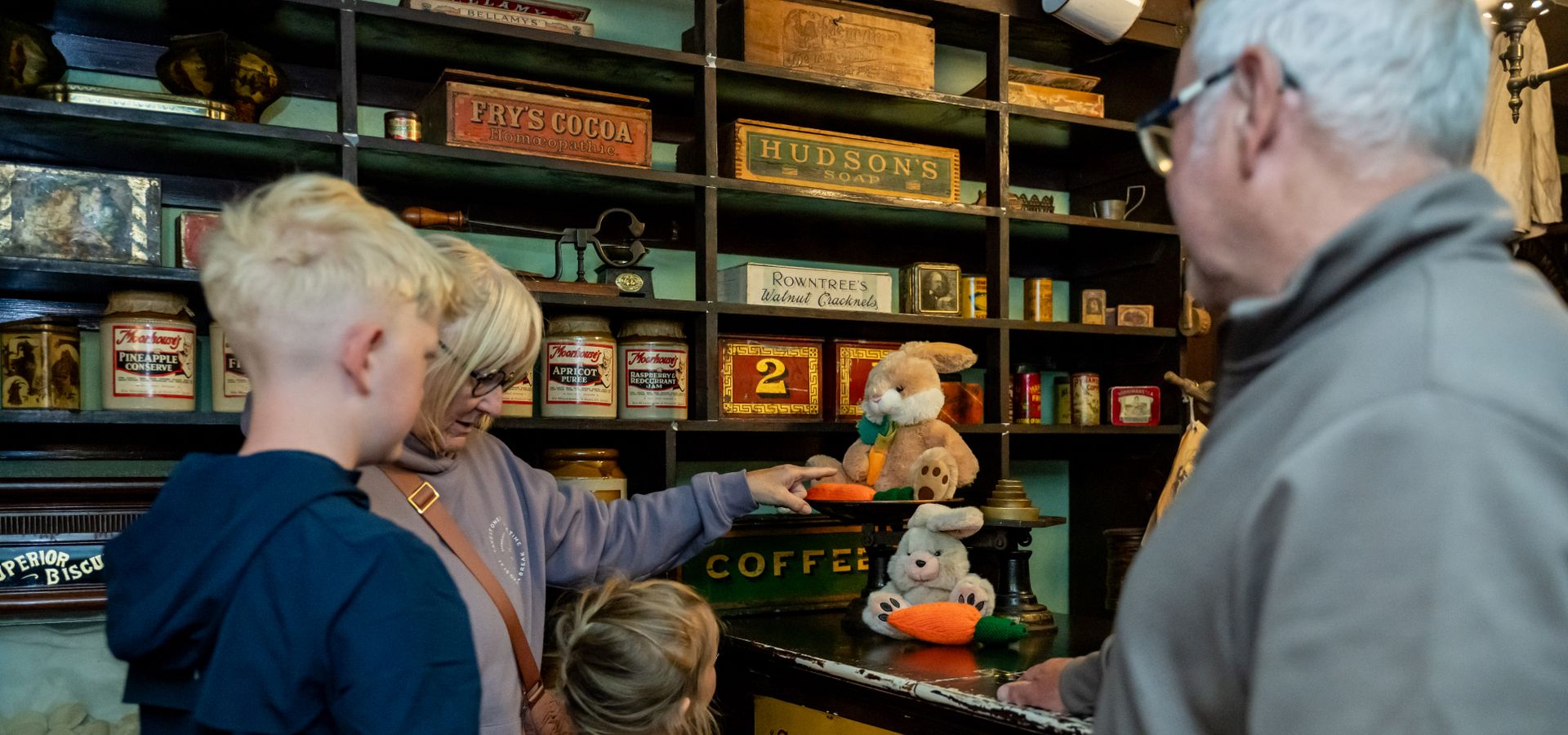 Two adults and 2 children looking at an old fashioned shop counter with rabbits on