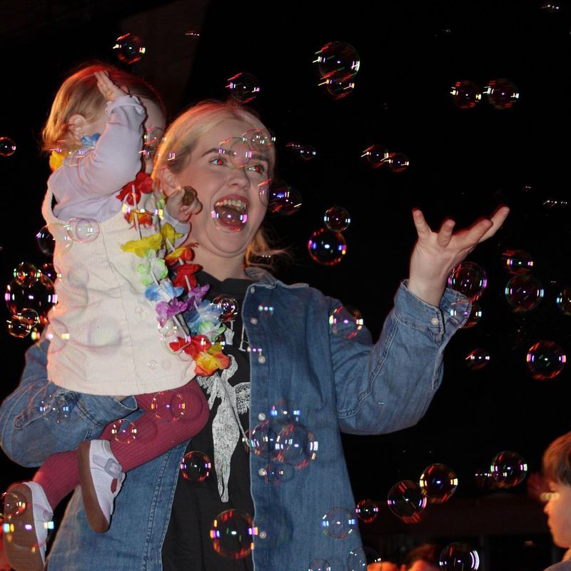 a parent holding a toddler playing with bubbles in a dark room