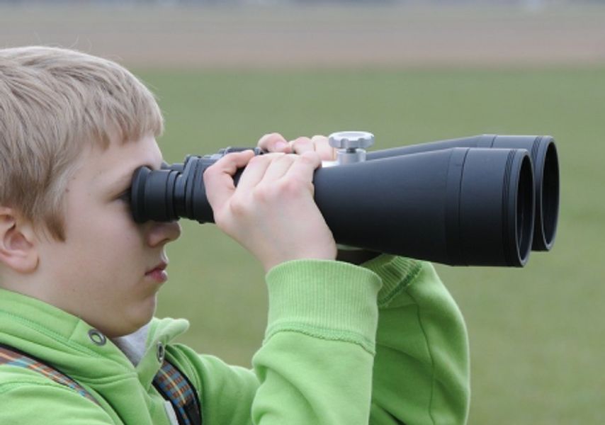 A child looks through binoculars in a field 