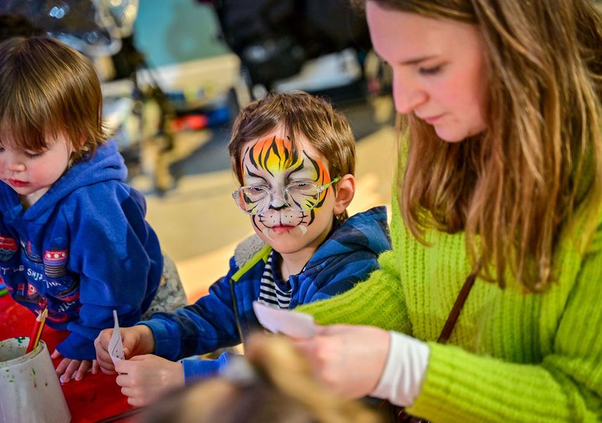 An adult and 2 children doing crafts with face paint on