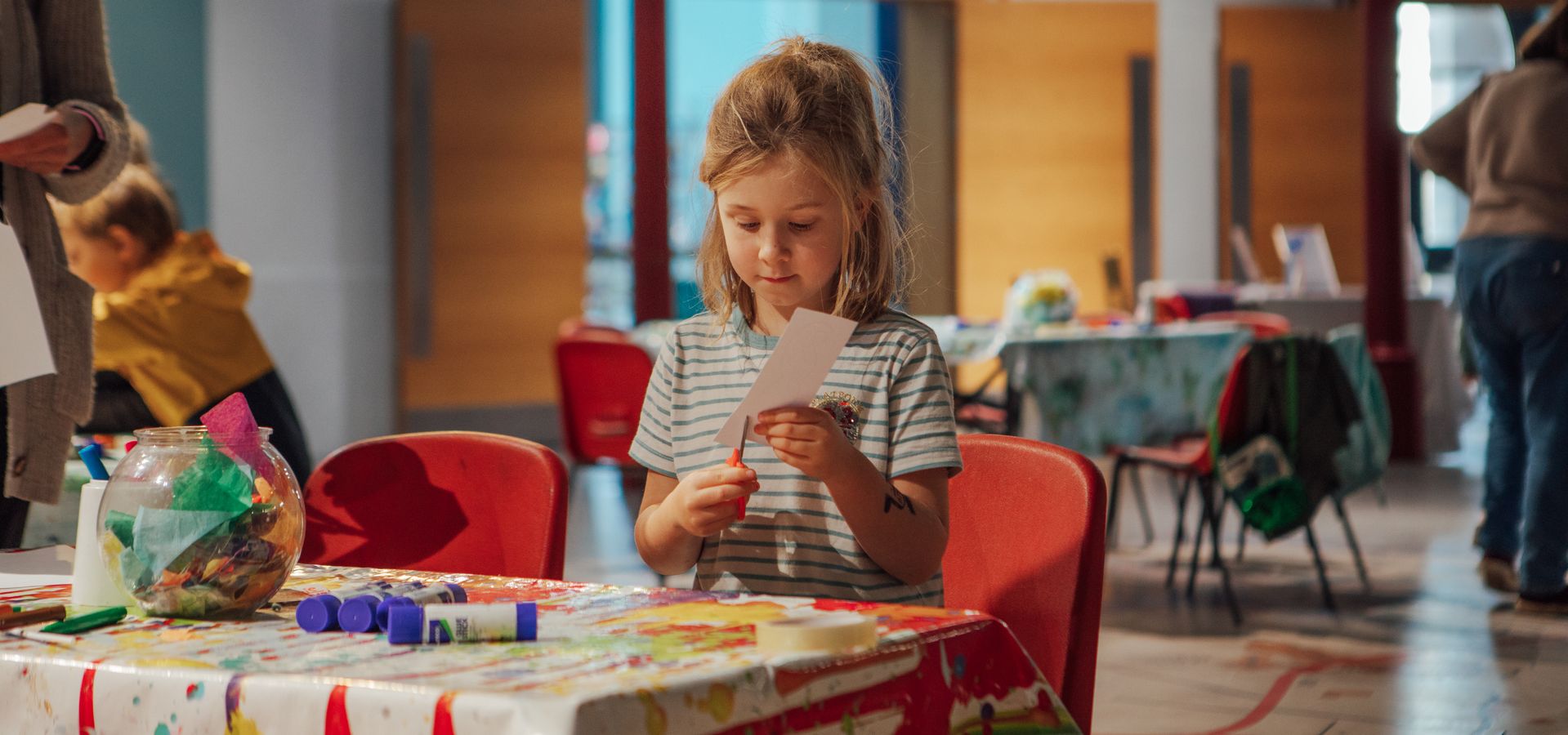 Girl at arts and crafts table, cutting paper.