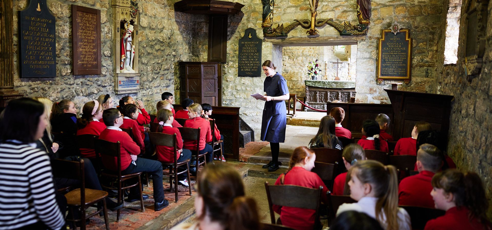 A teacher stood in front of rows of children in red school uniforms in the chapel