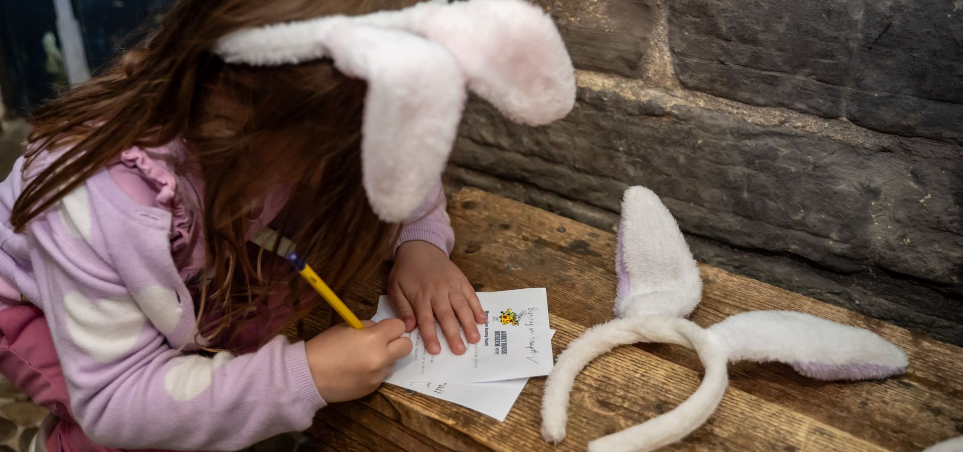 A child with bunny ears on looking at a trail sheet on a bench, next to another pair of bunny ears