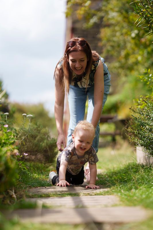 An adult leaning over a crawling child down a pathway