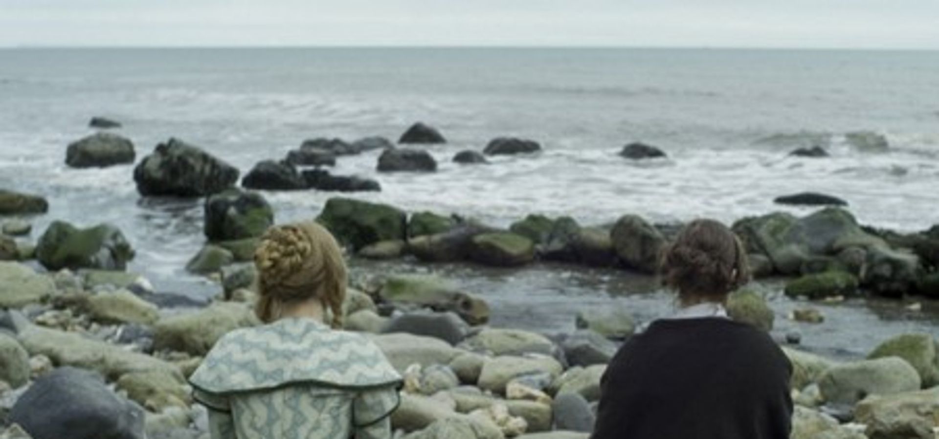 two women in 19th century costume sitting on a beach