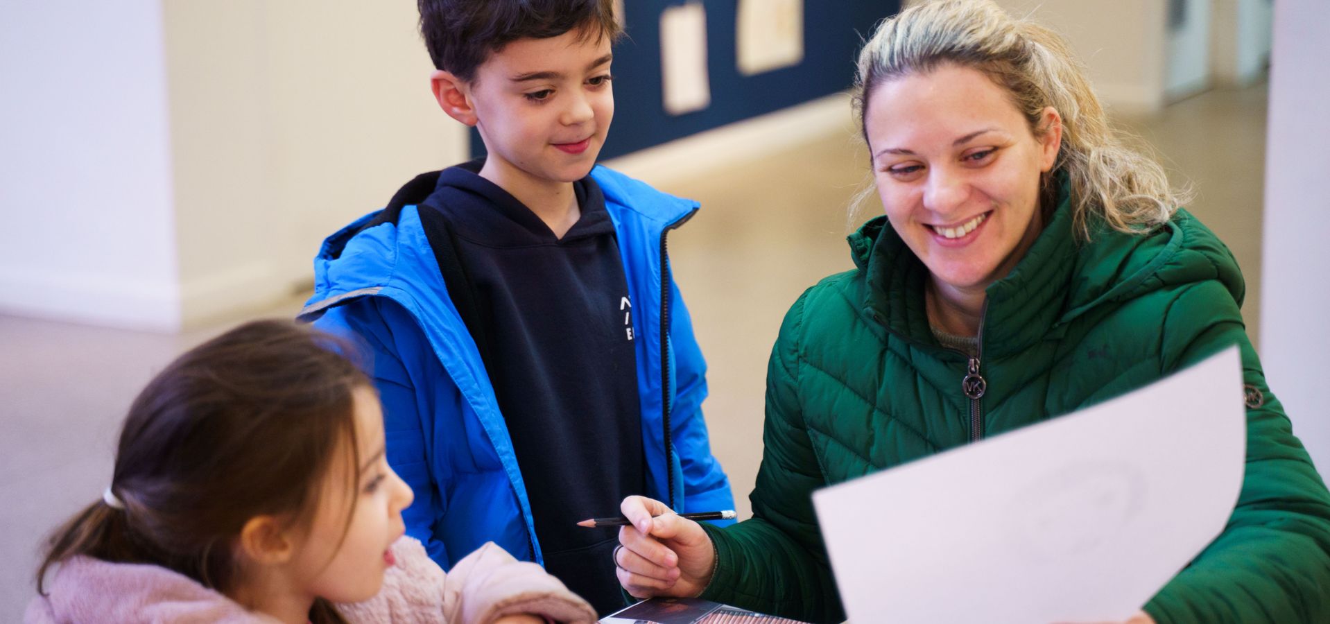 An adult and 2 children looking at drawing whilst sat at a table