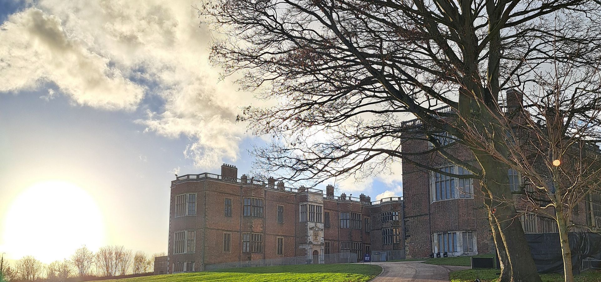 Temple Newsam House with the sun setting in the background and a path leading up to the house with a tree