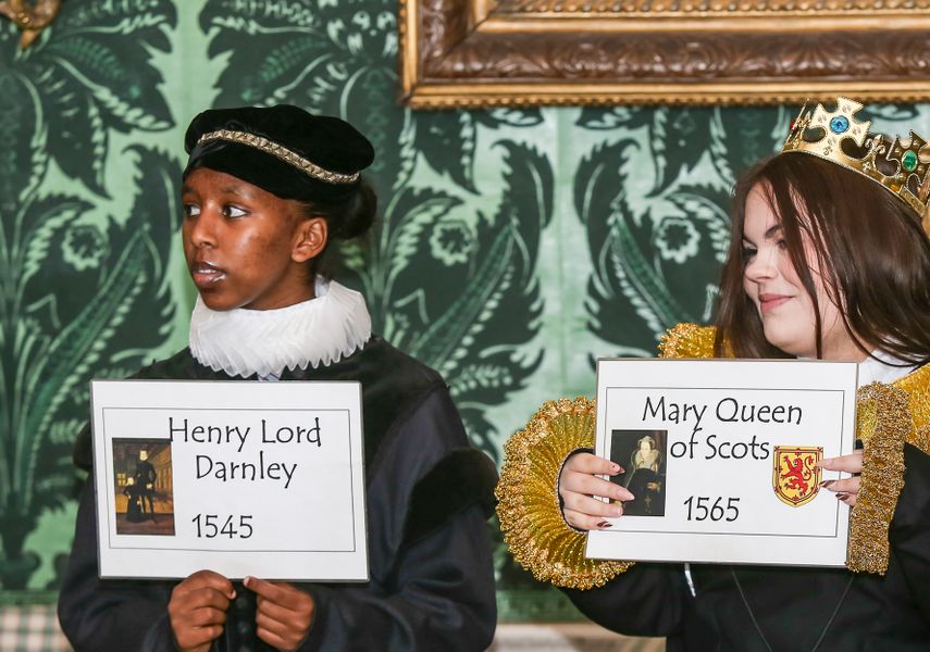 Two students in fancy dress, holding a sign each of who they are, 'Henry Lord Darnley' and 'Mary Queen of Scots'.