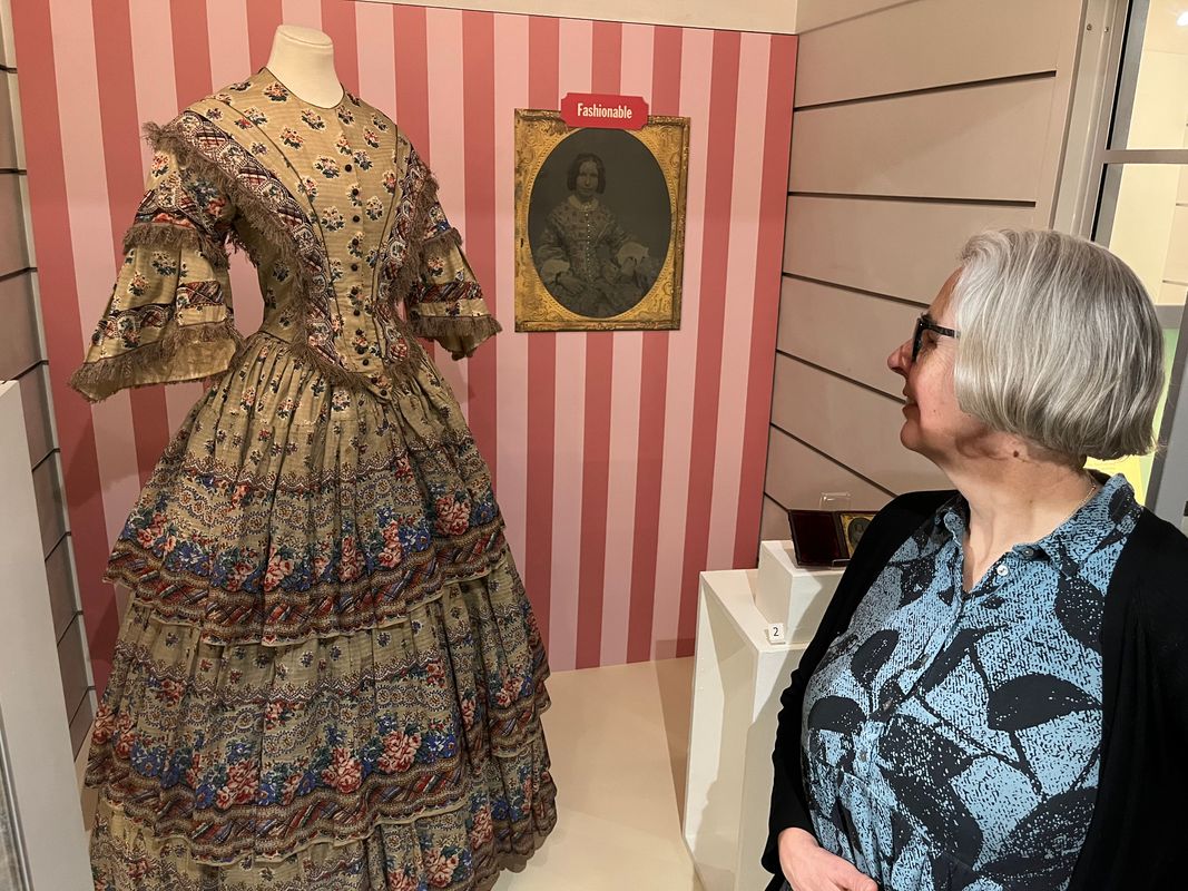 Curator Kitty Ross admires a beautiful printed cotton dress made in around 1855. The dress is on display as part of In the Picture at Abbey Housee Museum.
