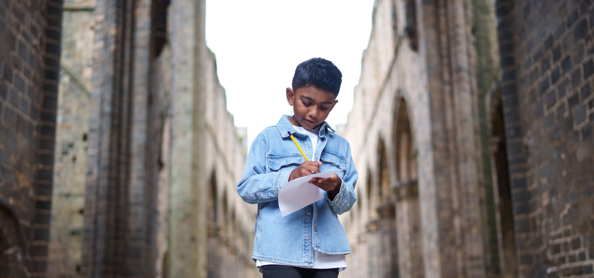 A child completing a worksheet surrounded by the ruins of Kirstall Abbey