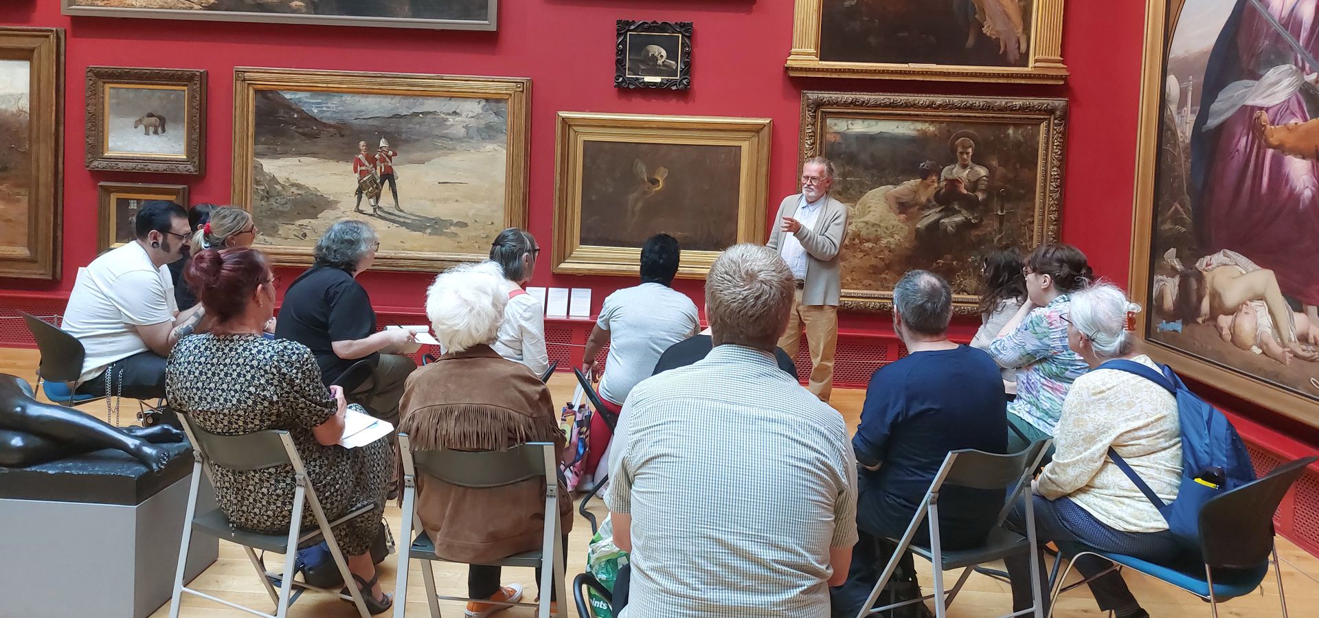 A group of people listening to a talk infront of a wall with artwork