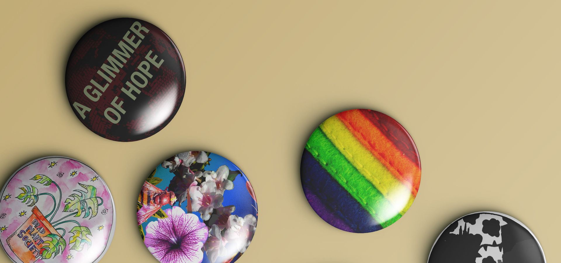 A collection of badges, including one that says 'A Glimmer of Hope, one with a house plant on, a fabric rainbow striped one and more in a beige background