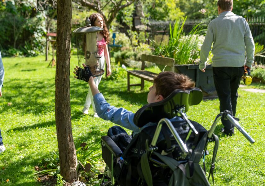 A child in a wheelchair looking at a bird feeder, with family looking around