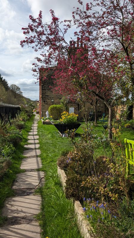 A pathway into a garden with an old building behind