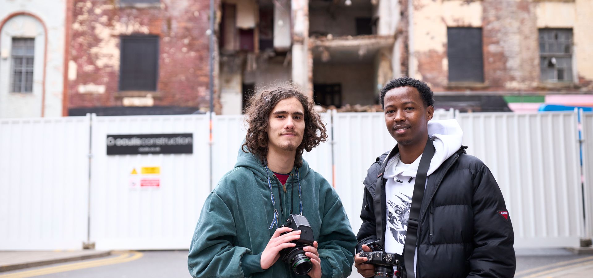 Two young adults stood in front of an abandoned building