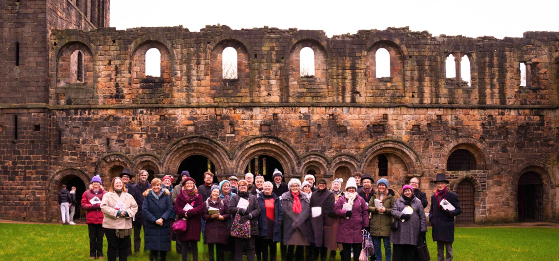 A choir group stood on grass with Kirkstall Abbey behind