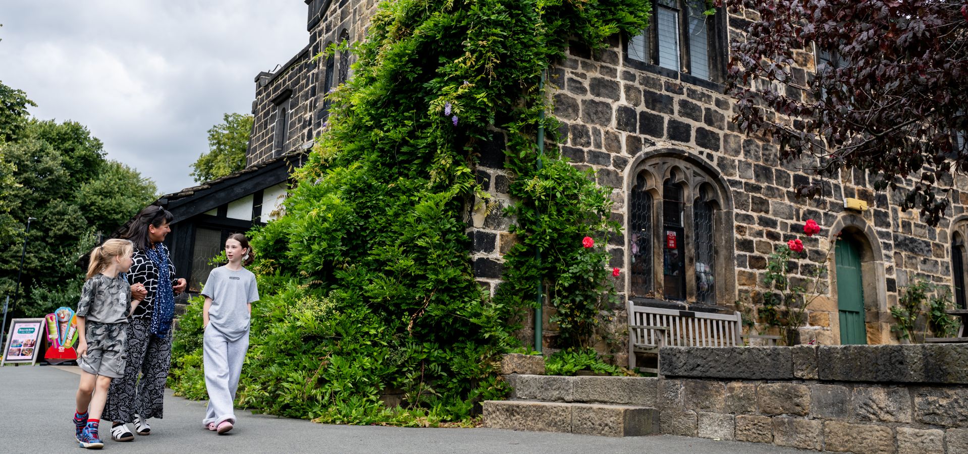 Three people walking infront of a building with a green bush growing up it