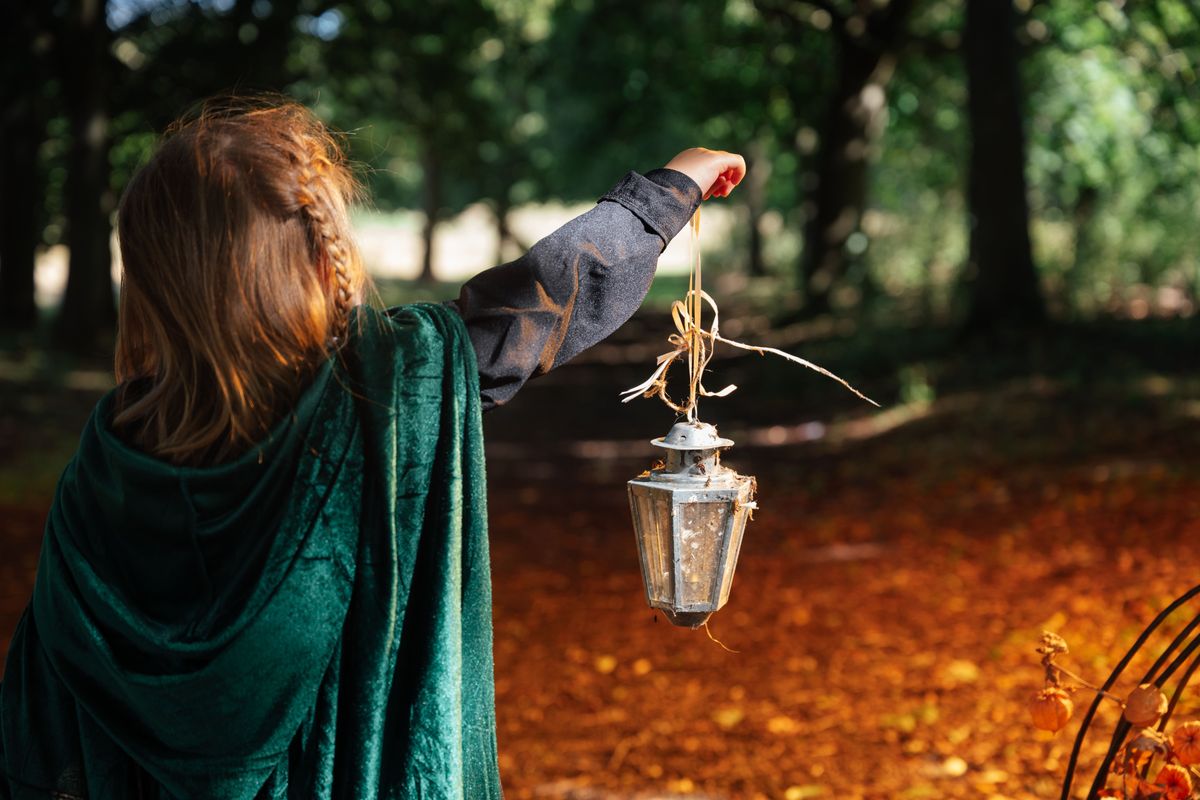 A child wearing a witch costume holding up a silver lantern
