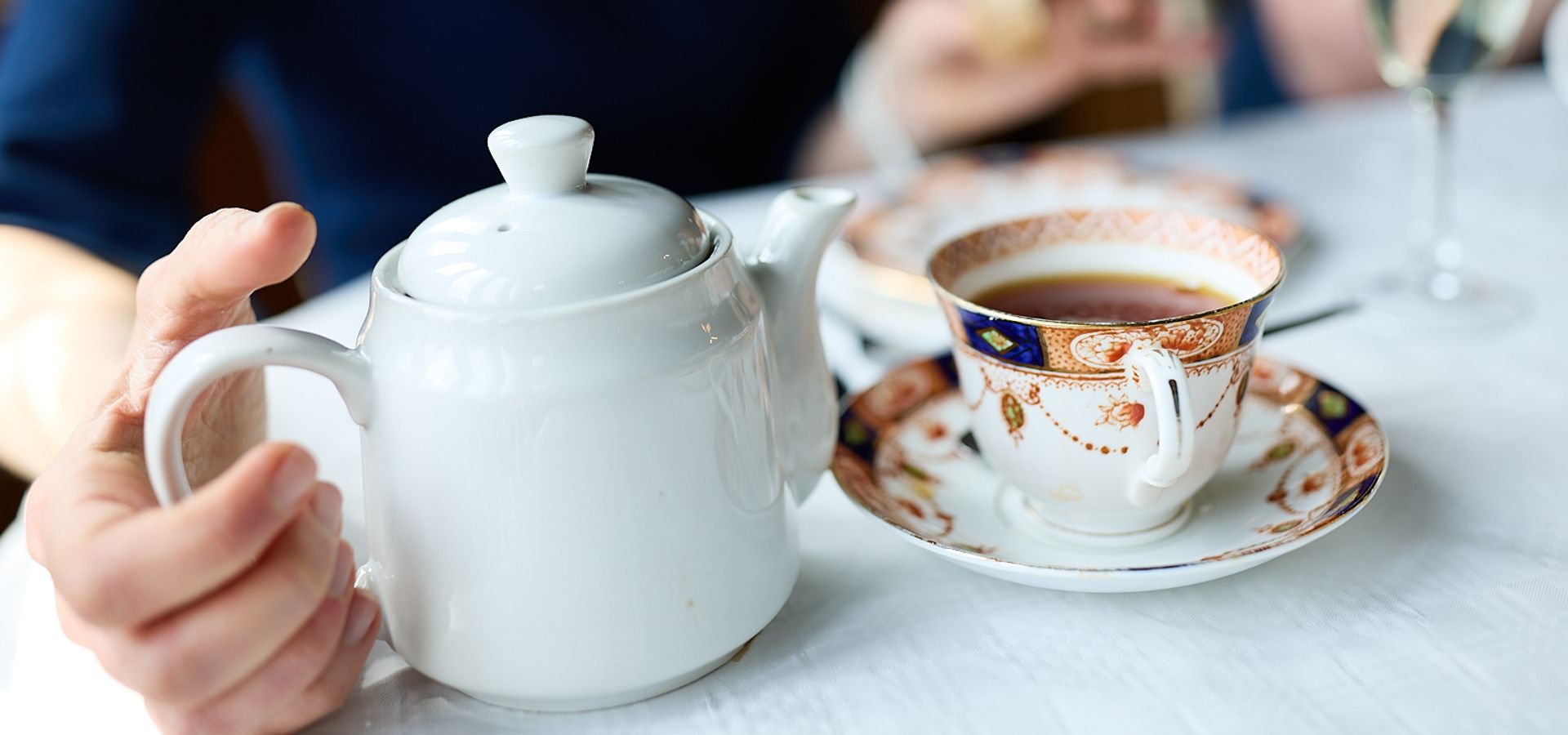 A hand reaching for a tea pot next to a china tea mug