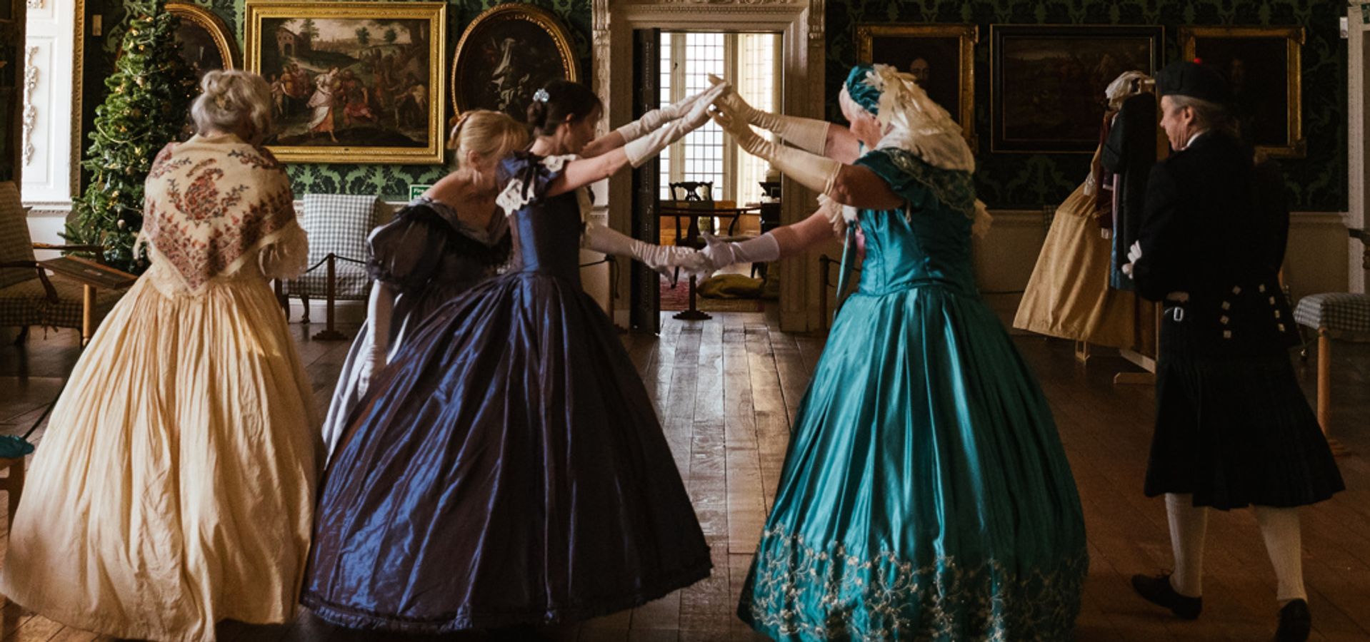 A group of dancers in long dresses with their arms reached up to make a tunnel