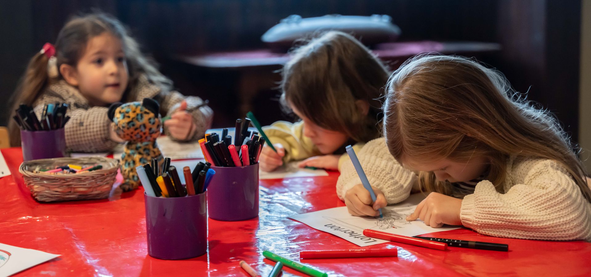 3 children sat at a table doing an activity on paper with coloured pens