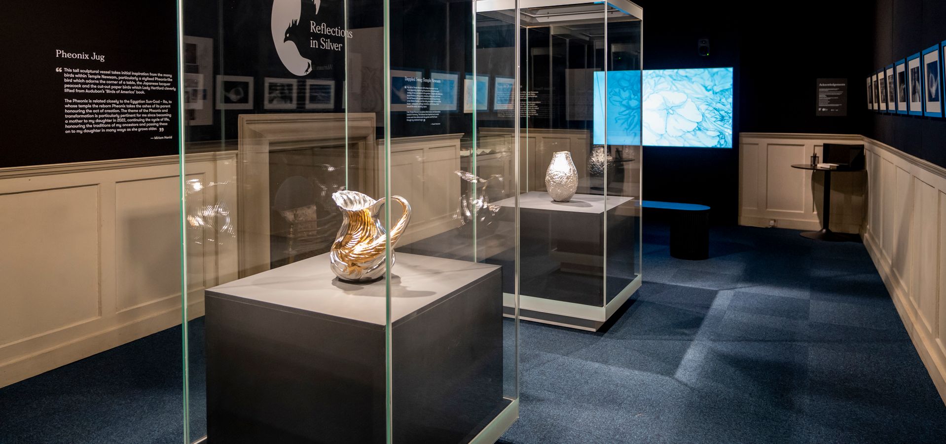 Two large display cabinets with silverware in them, with a screen at the back of the room