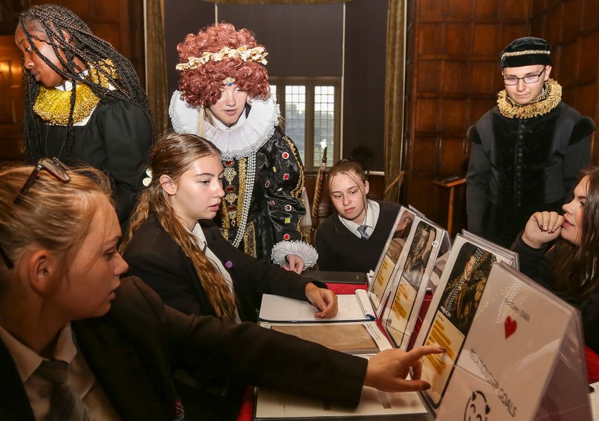 Students looking at activity sheets with people in Queen costumes behind