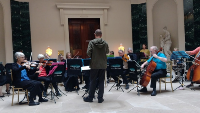 A conductor stands in front of a small orchestra with string instruments