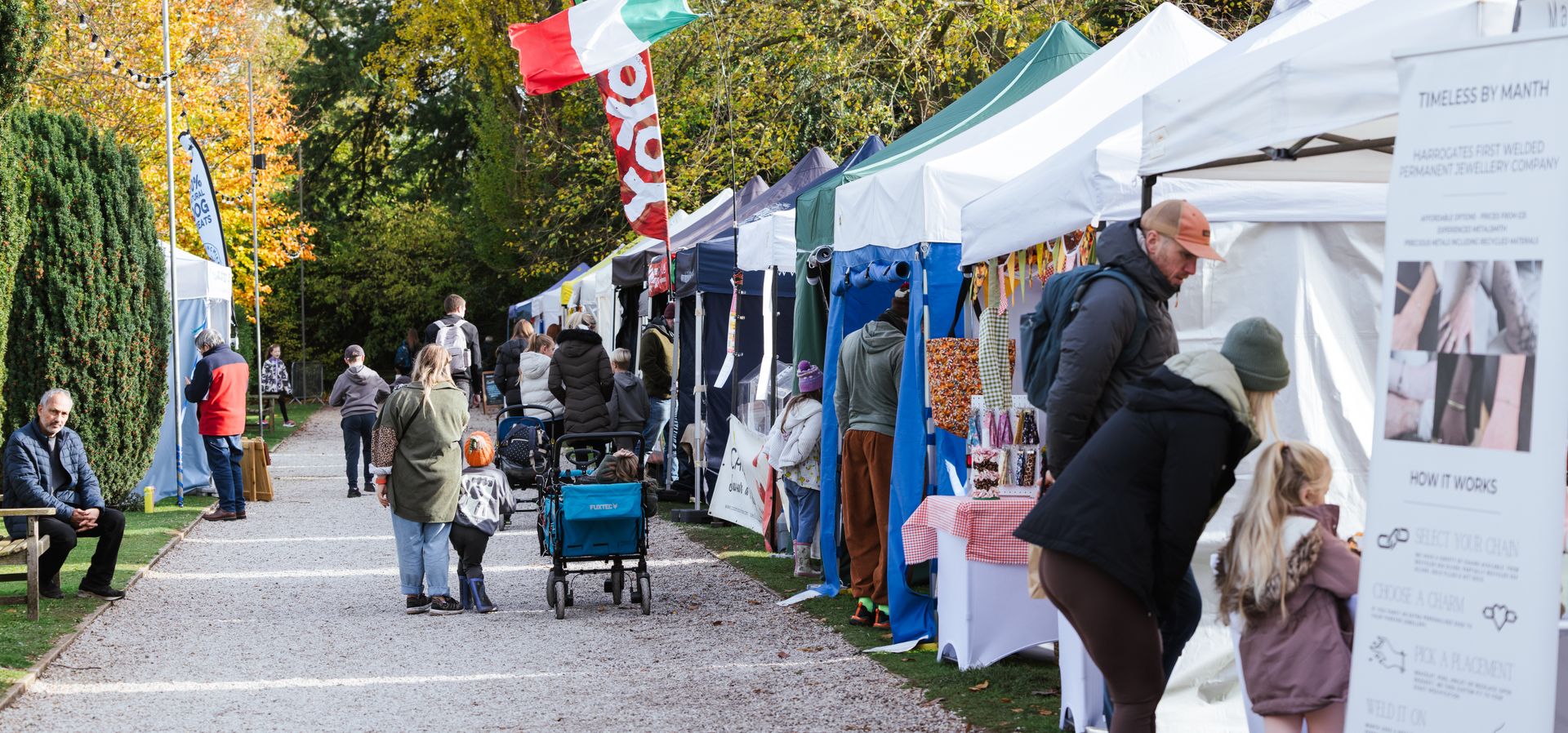 A pathway with a hedge on the left and white marquees with market stalls in on the right
