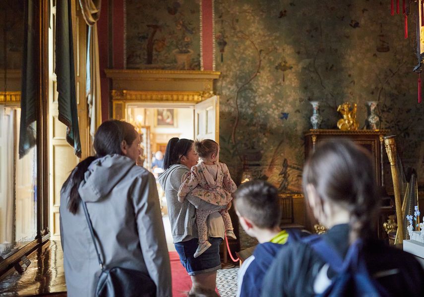 An adult holding a child and a family walking behind looking at the Chinese Room at Temple Newsam