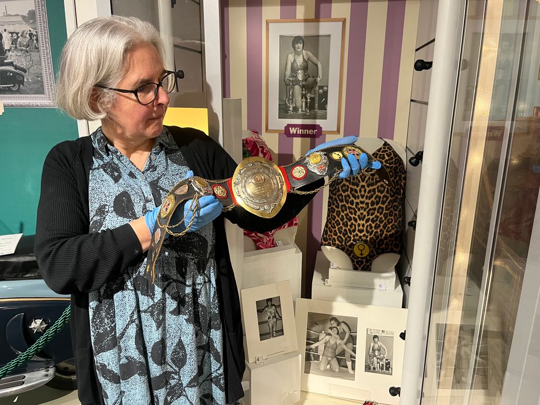 Curator Kitty Ross with a leotard and belt once worn by the city’s own female wrestler Sue Brittain, later known to opponents as Lady Satan. 