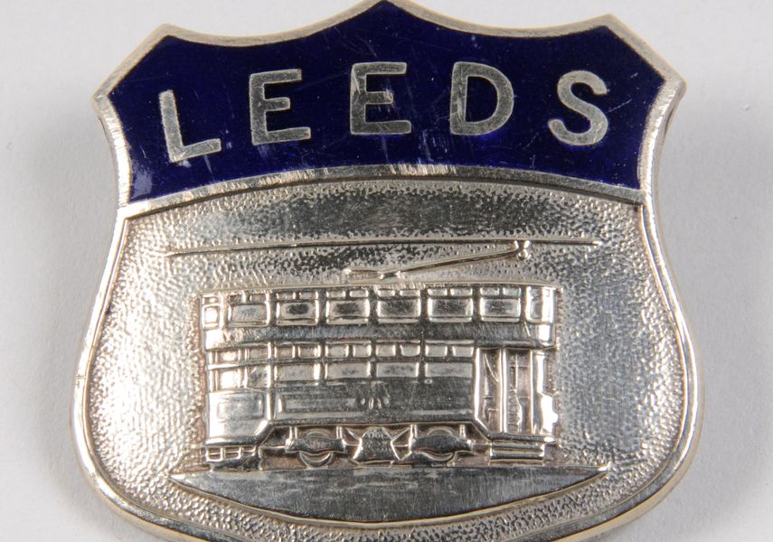 A silver badge with a tram and the word Leeds