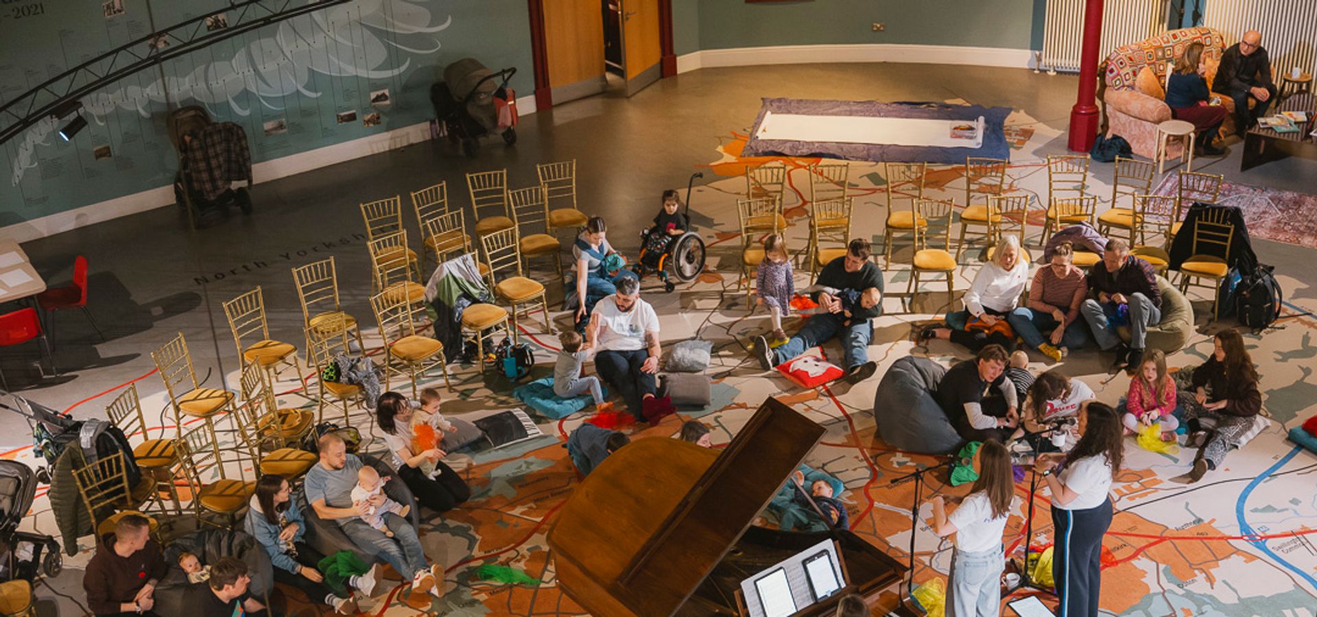 A photograph of families listening to live music performed by two vocalists and a pianist at a grand piano.