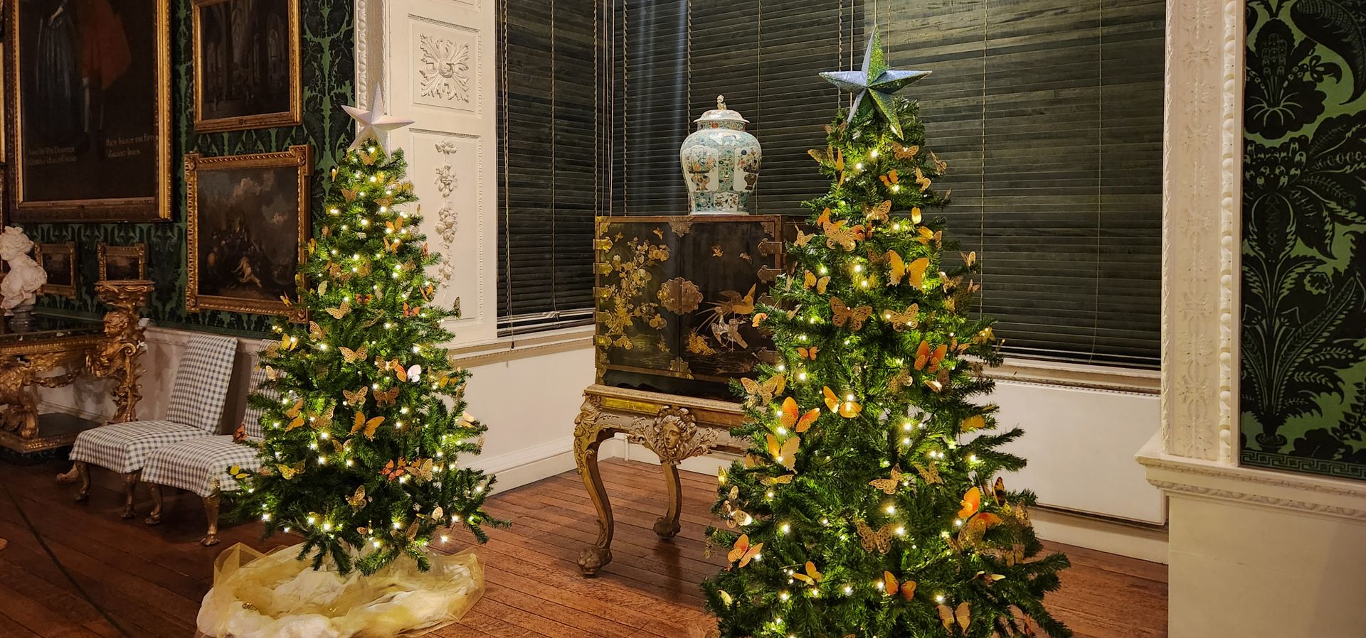 Two christmas trees covered in gold butterflies with a cabinet in between